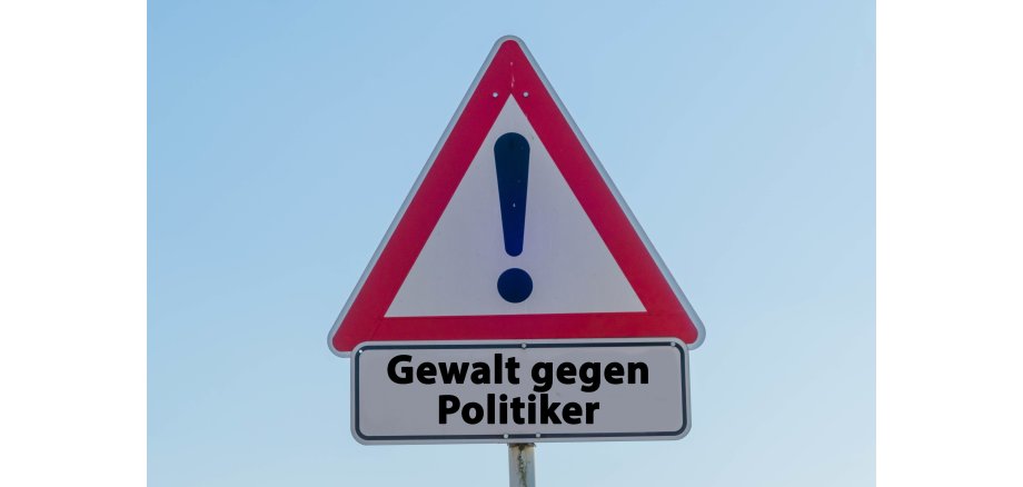 Das Bild zeigt ein Verkehrsschild mit einem Ausrufezeichen und dem Schriftzug "Gewalt gegen Politiker".