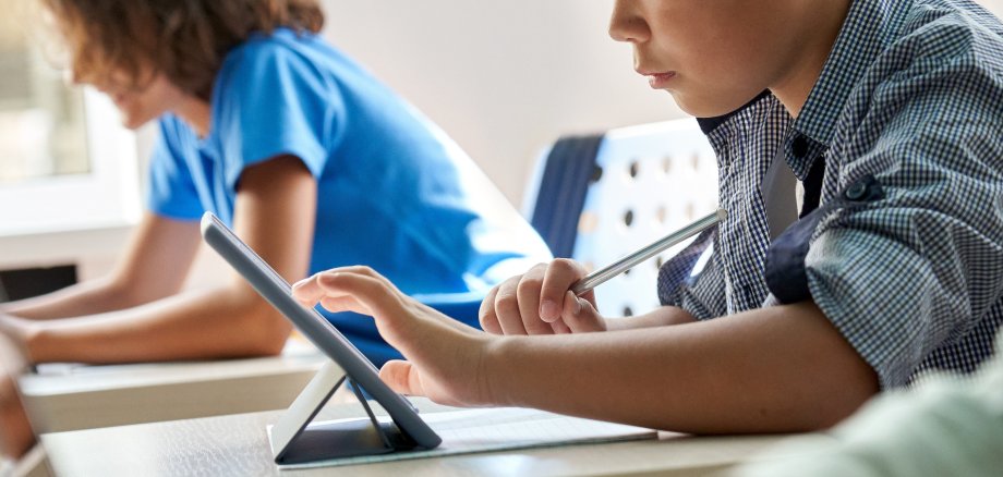 Das Foto zeigt einen Schuljungen mit einem Tablet in einem Klassenzimmer.