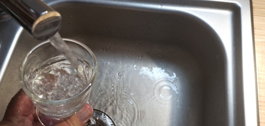 Das Foto zeigt ein Glas, das mit Wasser aus einem Wasserhahn befüllt wird.